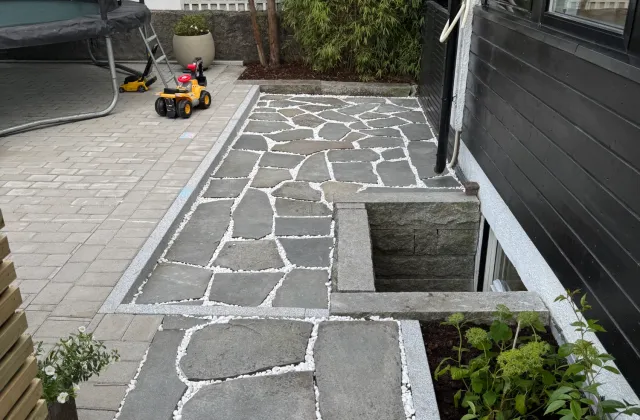 Bruddskifer med hvit singel i fugene, granittkantstein og belegningsstein ved husvegg