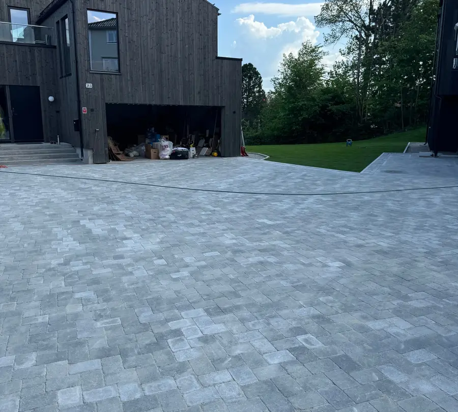 Ferdig gårdsplass i grå belegningsstein foran svart trehus