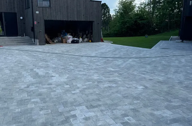Ferdig gårdsplass i grå belegningsstein foran svart trehus