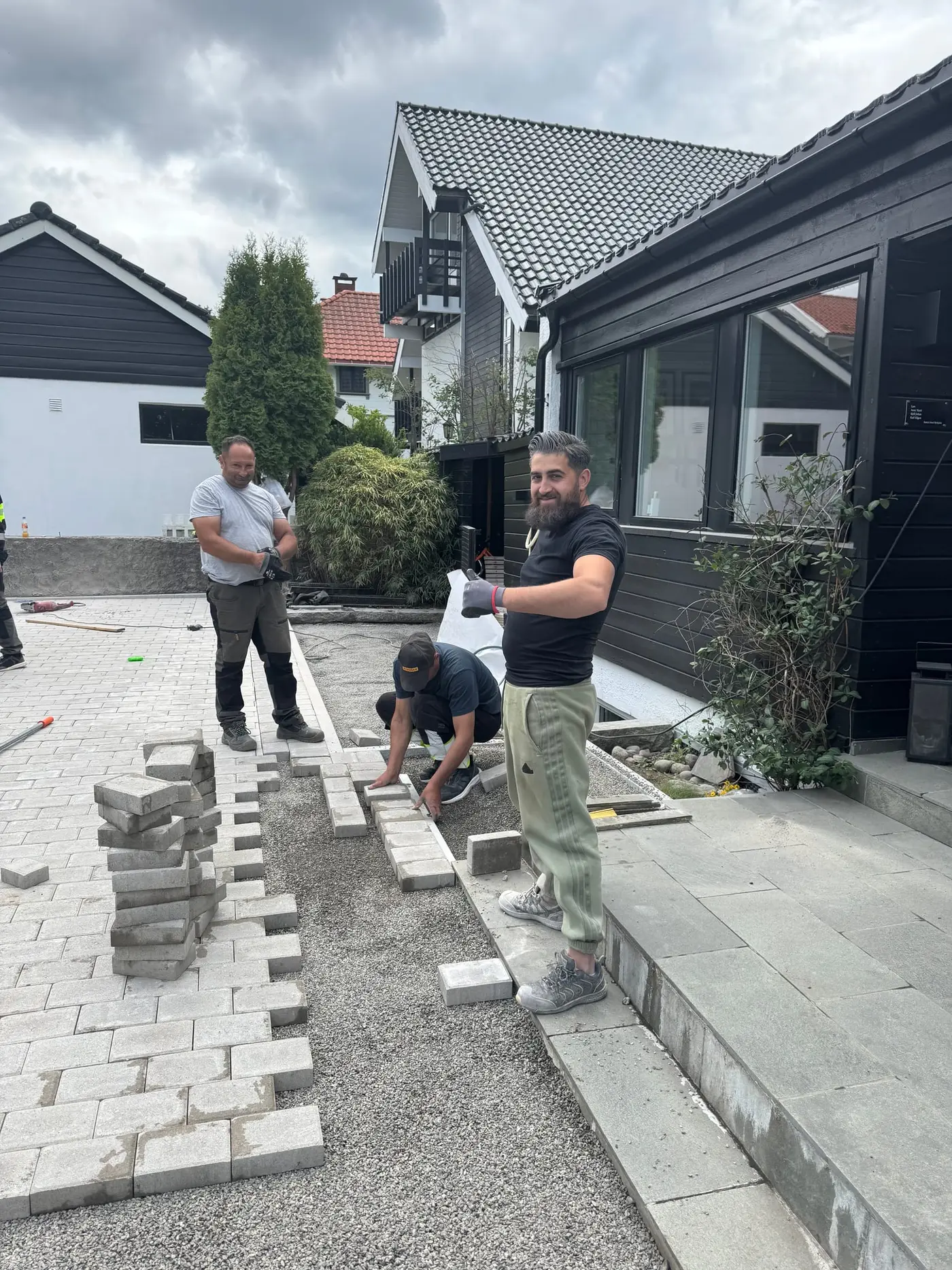 Tre av våre folk legger grå belegningsstein langs mørkt hus