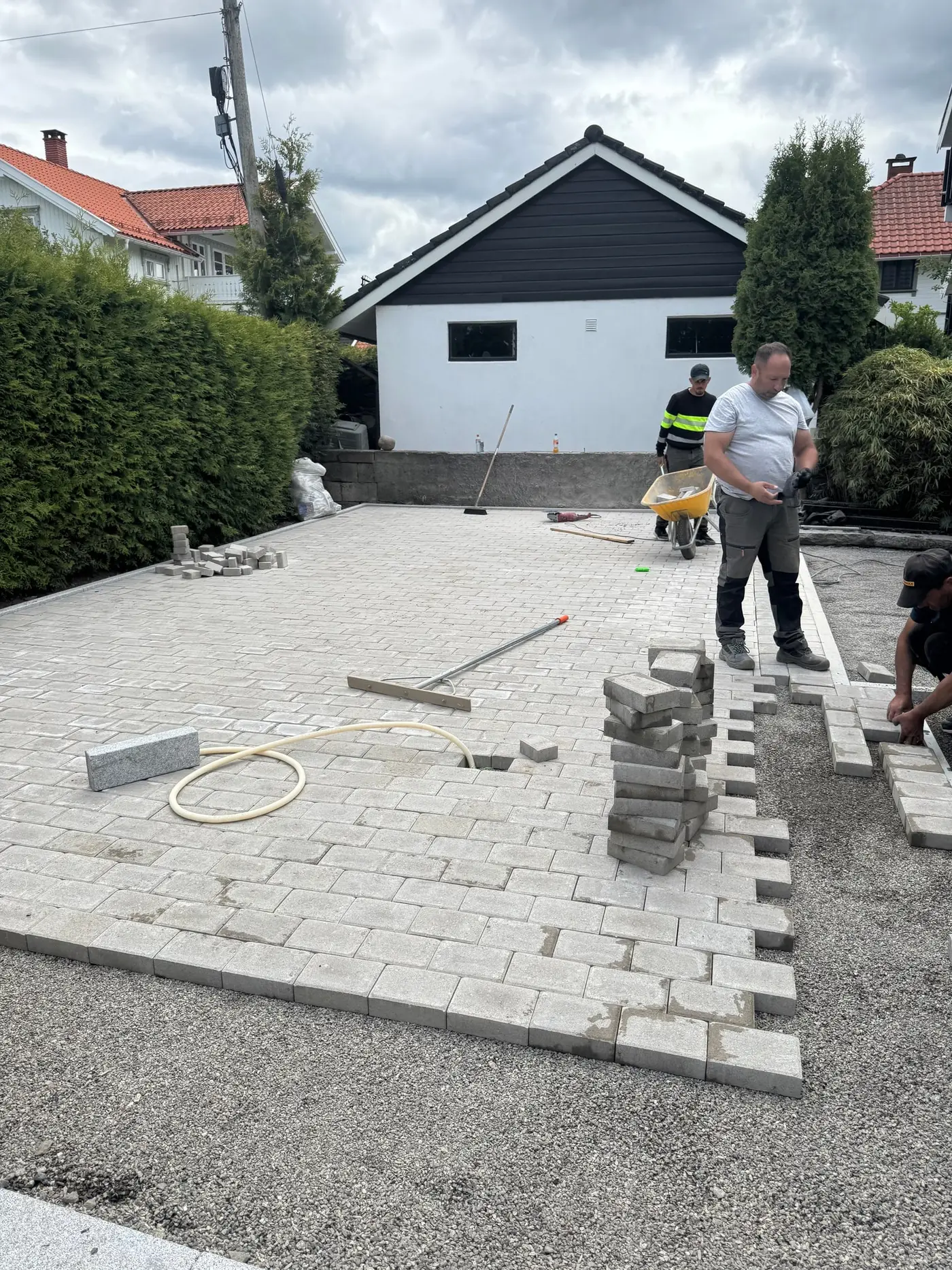 Arbeidere legger lys grå belegningsstein i løpeforband på stor gårdsplass