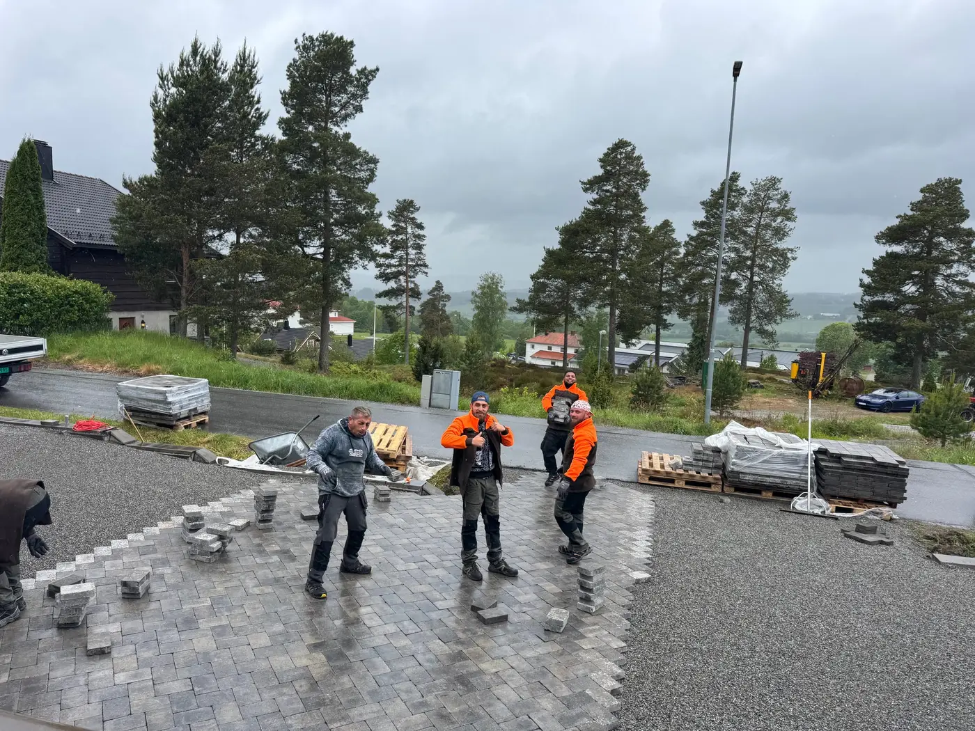 Fire av våre folk legger belegningsstein på stor oppkjørsel i regnvær