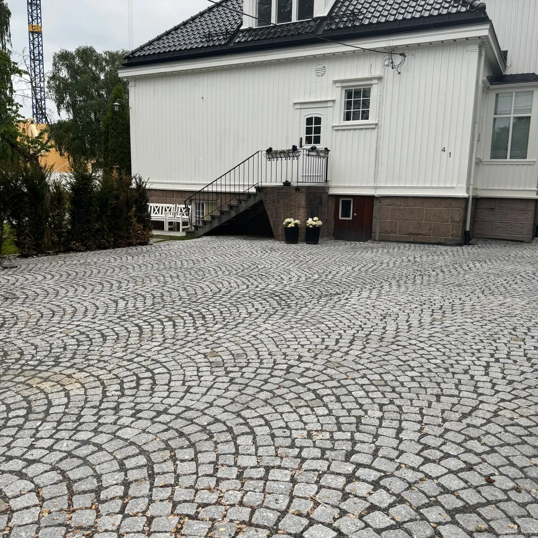 Ferdig brosteinsplass i buemønster foran stor hvit villa