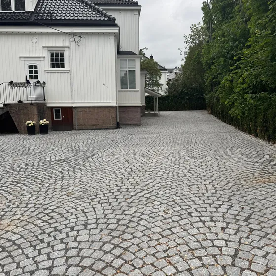 Gårdsplass i granitt smågatestein lagt i buemønster foran hvitt hus