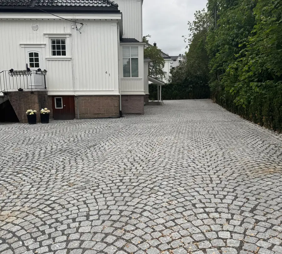 Gårdsplass i granitt smågatestein lagt i buemønster foran hvitt hus