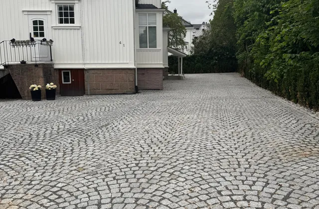 Gårdsplass i granitt smågatestein lagt i buemønster foran hvitt hus