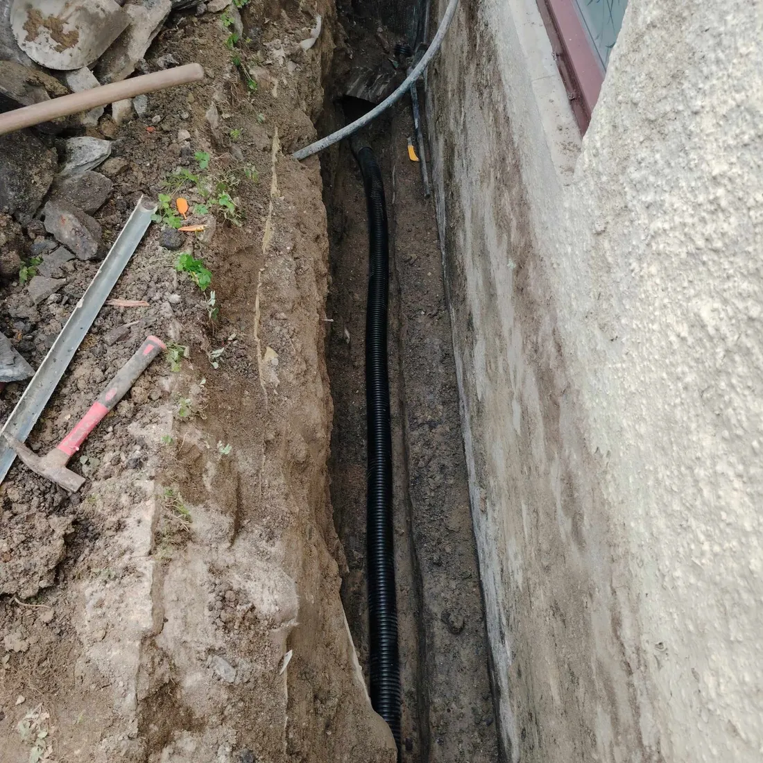 Grøft langs grunnmur med nytt drensrør og kabel lagt i bunnen
