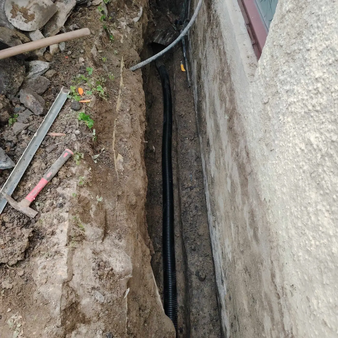 Grøft langs grunnmur med nytt drensrør og kabel lagt i bunnen