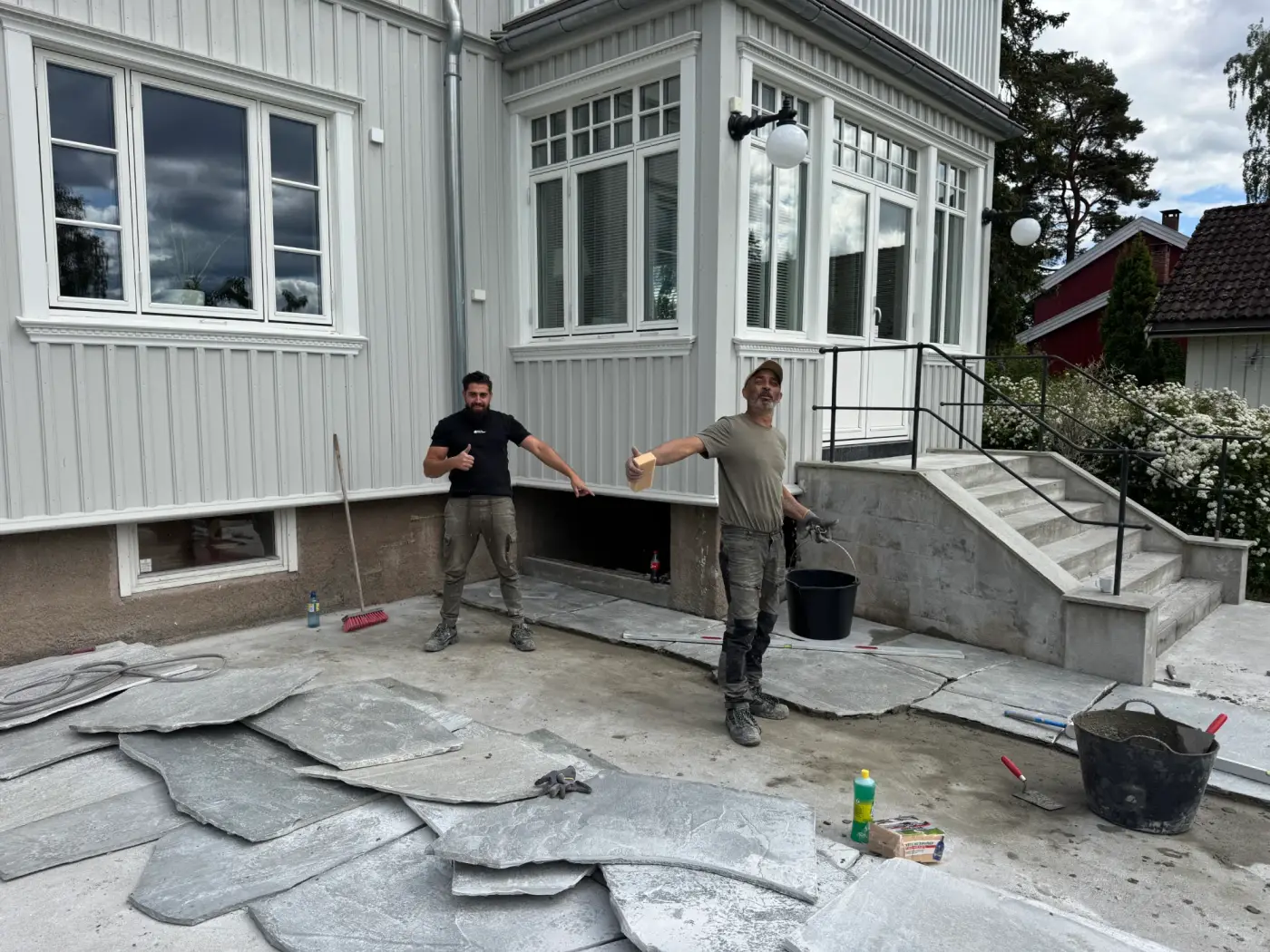 Anlegging av skifertegning på terrasse foran hvitt hus under konstruksjon.