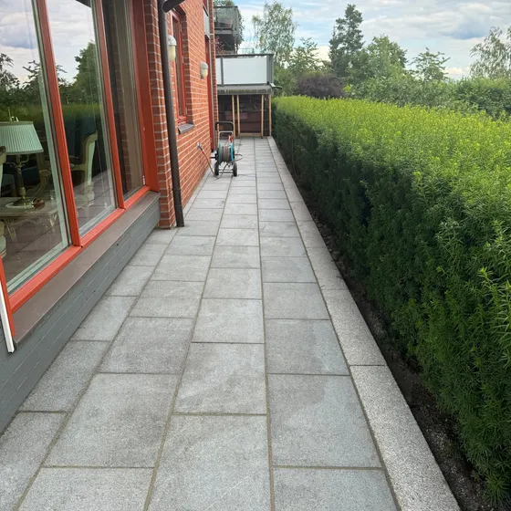 Smal hellelagt gangsone langs husvegg med hekk og granitt kantstein