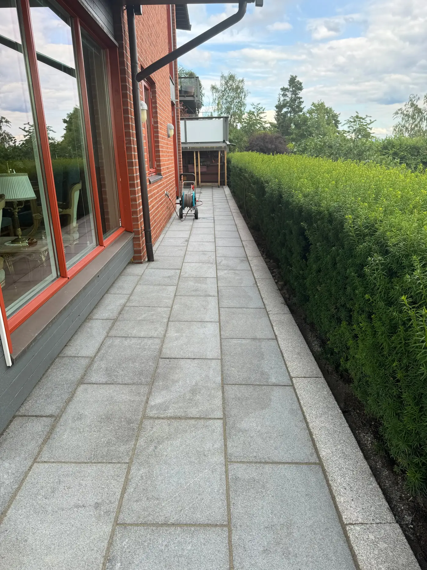 Smal hellelagt gangsone langs husvegg med hekk og granitt kantstein