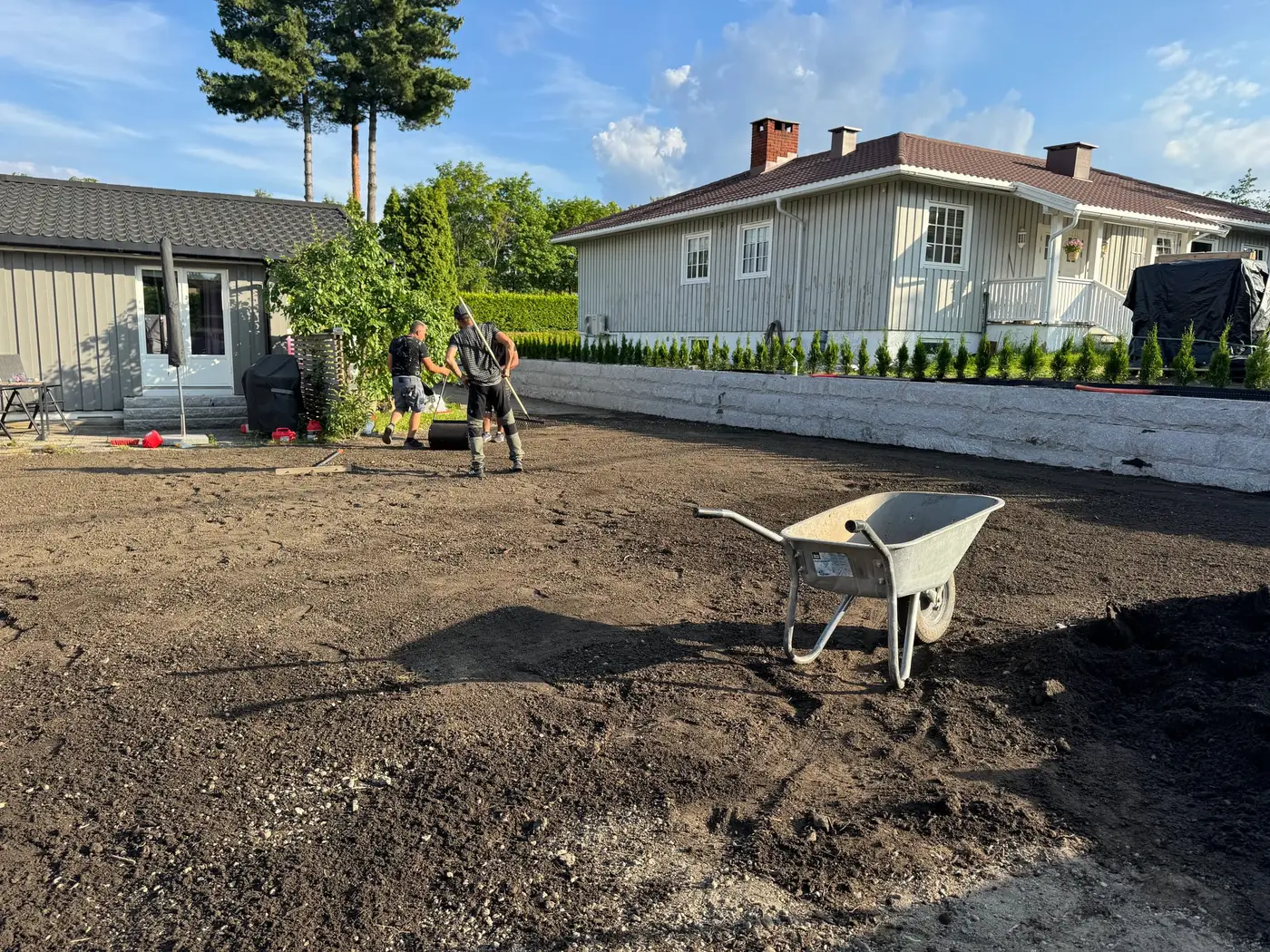 Arbeidere planerer og finavretter jordflaten før plenen legges