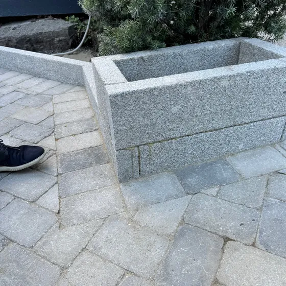 Plantekasse og lav kant i sagde granittblokker inntil steinlagt gårdsplass