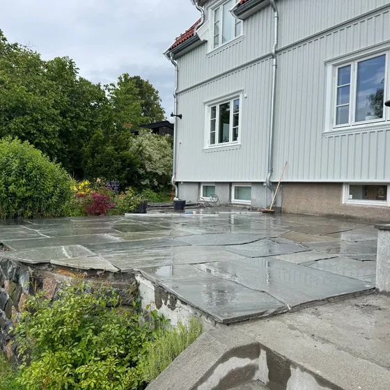 Skiferterrasse båret av kampesteinsmur mot plen