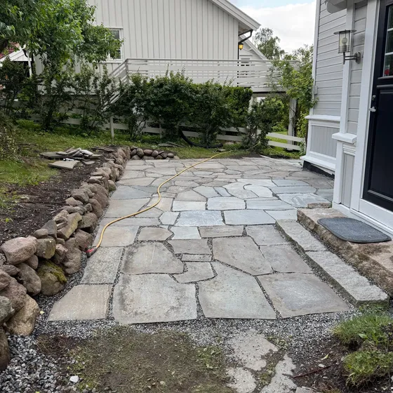 Uteplass i naturskifer med grusfuger og tørrmur av rullestein