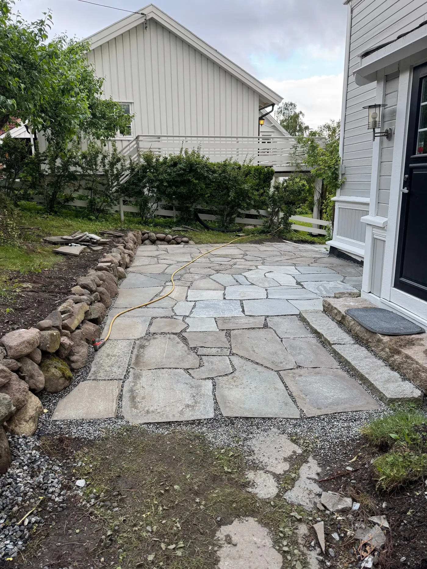 Uteplass i naturskifer med grusfuger og tørrmur av rullestein