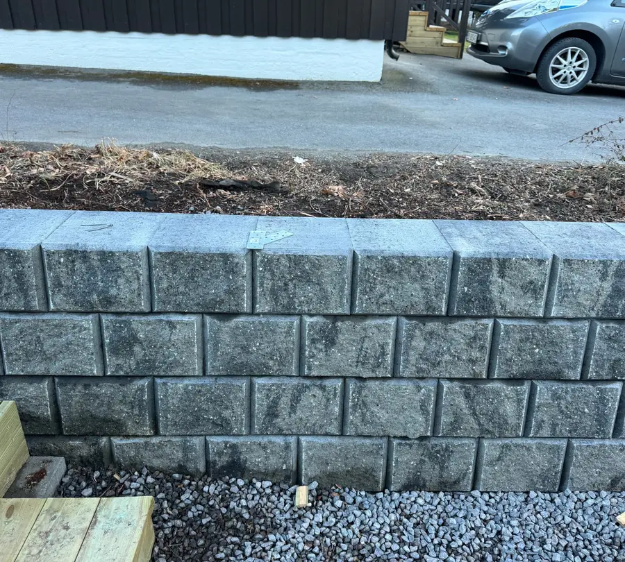 Ferdig støttemur i grå betongblokk med topphelle og pukkstripe foran